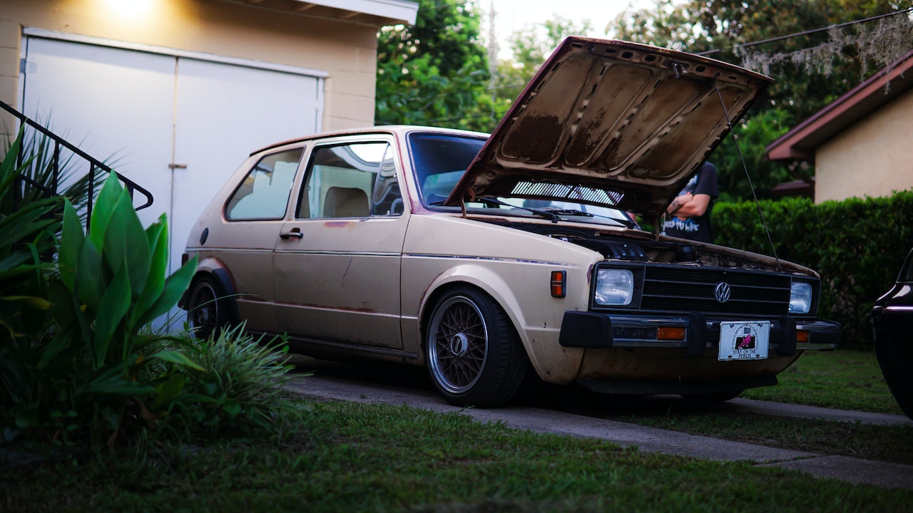 a Picture of a vintage Volkswagen Golf in a driveway with it's hood up.
