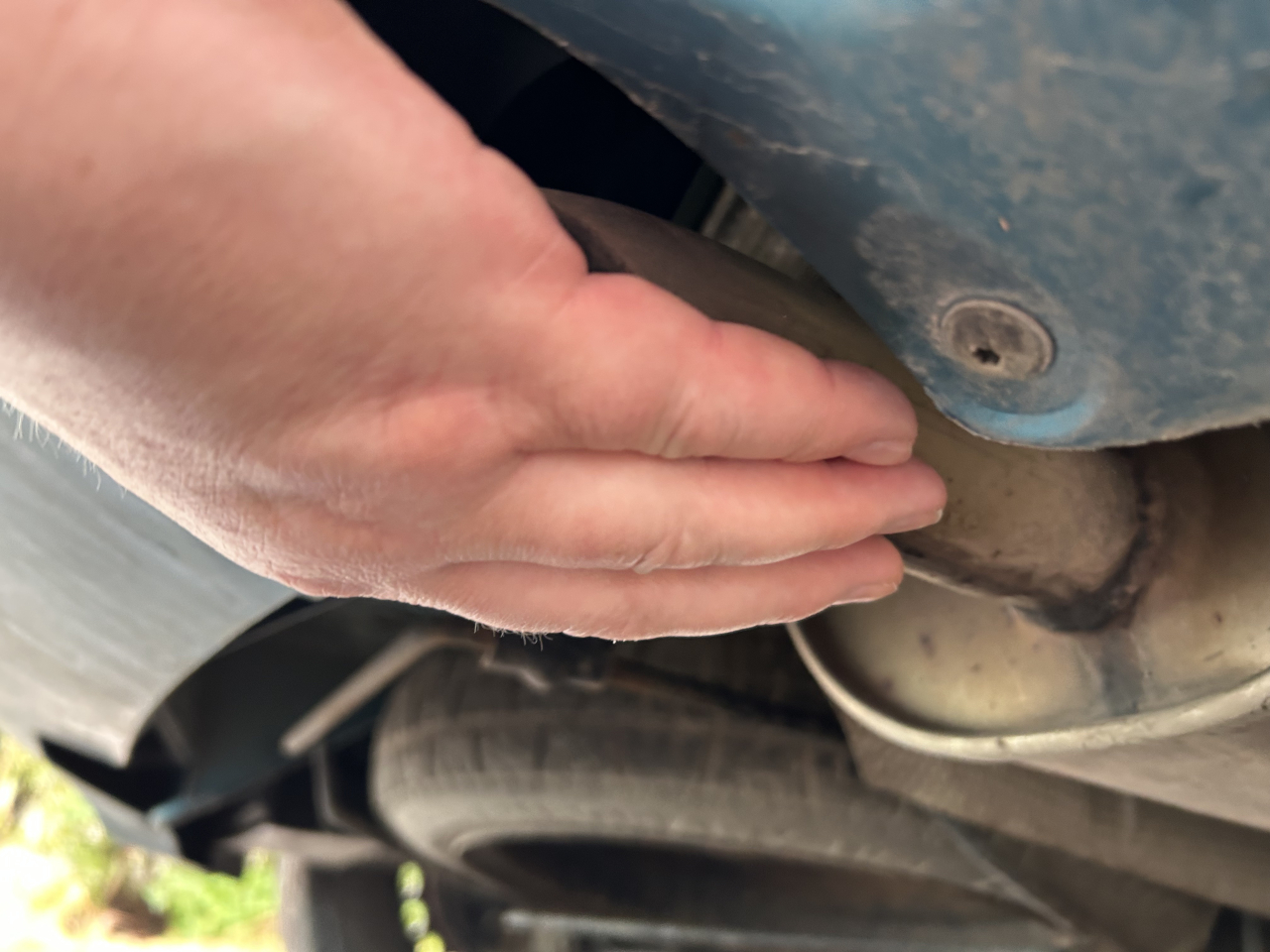 A Picture of a hand covering a car’s exhaust pipe while feeling the engine’s rhythmic put, put, put.